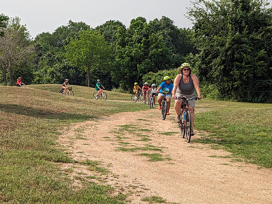 An adult leads children on bikes over a gravel road